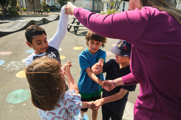 Four children hold hands in a knot activity with their teacher in the playground